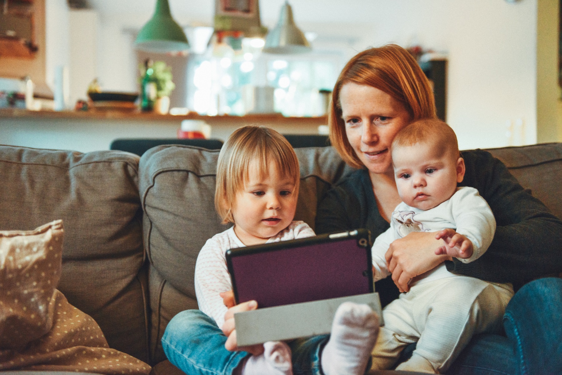 Mutter mit Kleinkindern und Tablet auf der Couch.